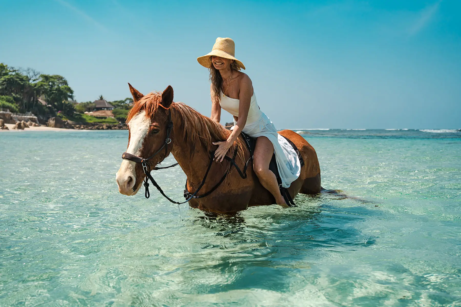 A guest riding a horse through clear ocean water at NIHI Sumba